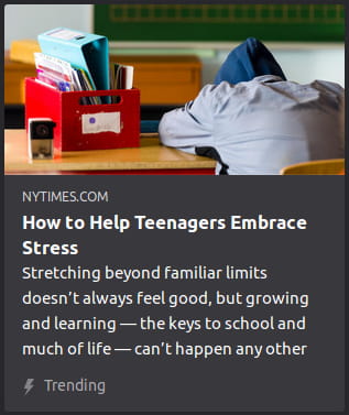 By NYTimes. Photo o’ a student with their back to the camera & their hood-covered face down in their arms on the desk next to a plastic red bin full o’ binders & composition books.